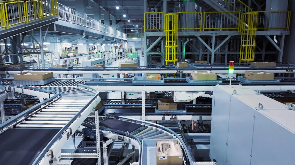 C'est une photo d'un centre de distribution moderne avec des tapis roulants automatisés transportant des colis, soulignant la complexité et l'efficacité de la logistique moderne.