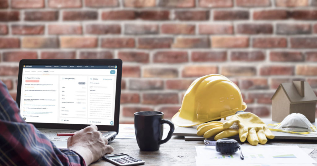 Image d'une personne travaillant sur un ordinateur portable affichant un rapport de maintenance, avec des équipements de sécurité de chantier tels qu'un casque et des gants posés à côté, illustrant la création et l'analyse de rapports de maintenance.