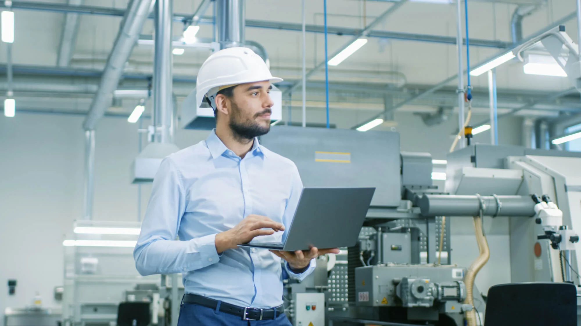 Un homme en casque de sécurité utilise un ordinateur portable dans une usine, illustrant les avantages de la maintenance corrective.