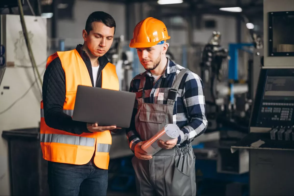 2 hommes en tenu de travail fluo orange devant un ordinateur dans une usine