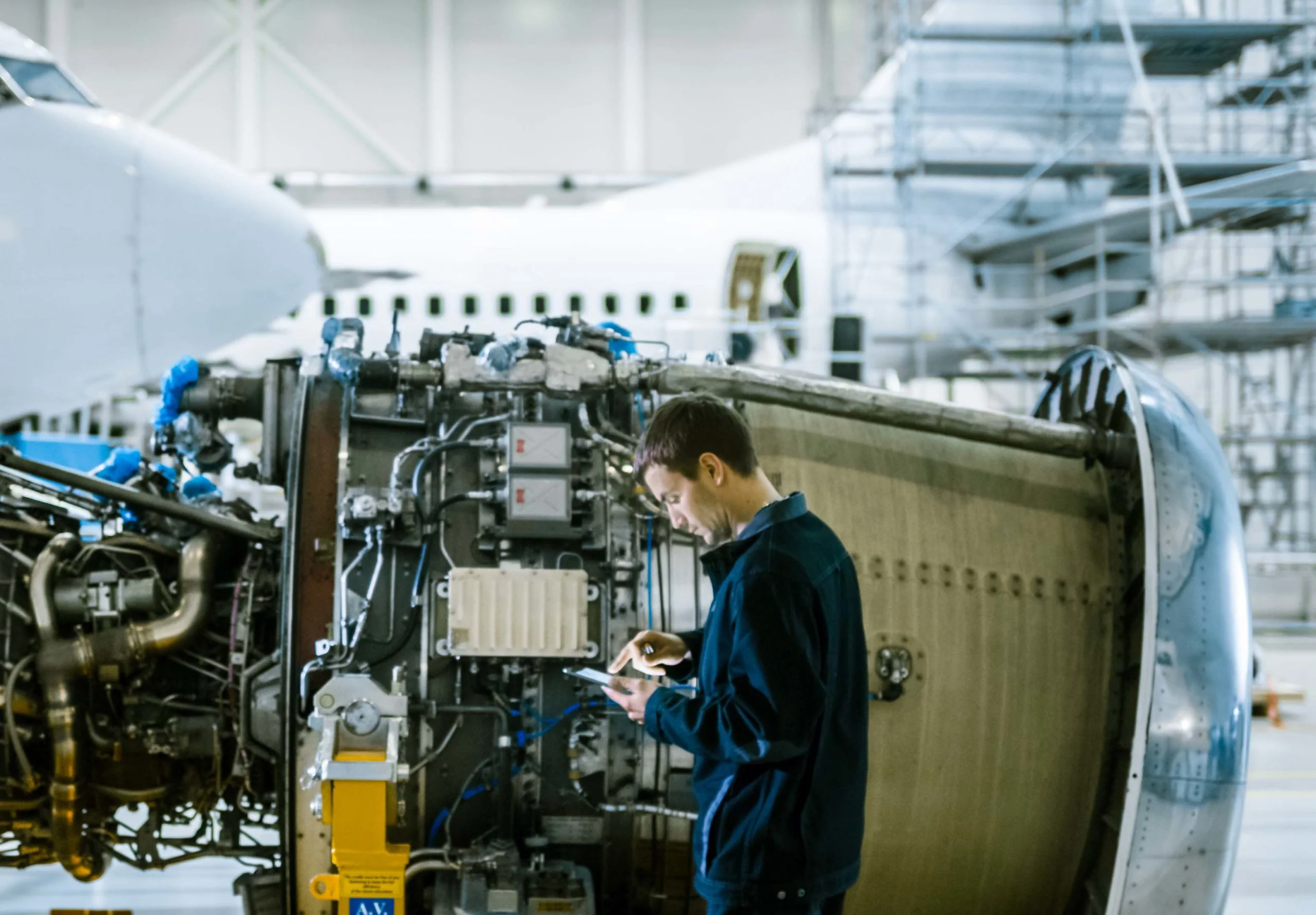 Un technicien inspecte un moteur d'avion tout en consultant une tablette, illustrant l'application de la méthode AMDEC (Analyse des Modes de Défaillance, de leurs Effets et de leur Criticité) dans l'industrie aéronautique pour identifier les risques potentiels et améliorer la fiabilité des systèmes critiques.